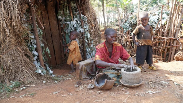 Burundilainen nainen valmistaa saviruukkua pihalla, vieressä pieni poika ja pieni tyttö.