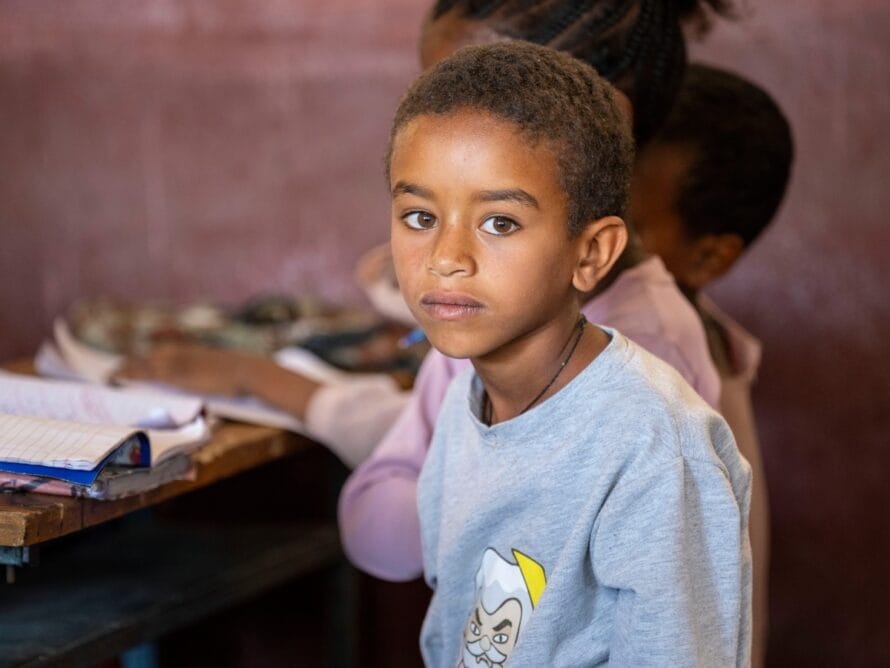 Koululaispoika istuu pulpetin ääressä ja katsoo kameraan.