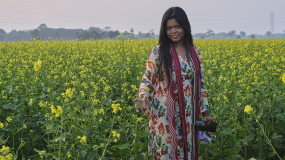 Bangladeshilainen nuori nainen seisoo rypsipellon keskellä.