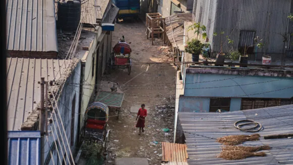 Tyttö kävelee punaisissa vaatteissa Bangladeshilaisen slummin kadulla.