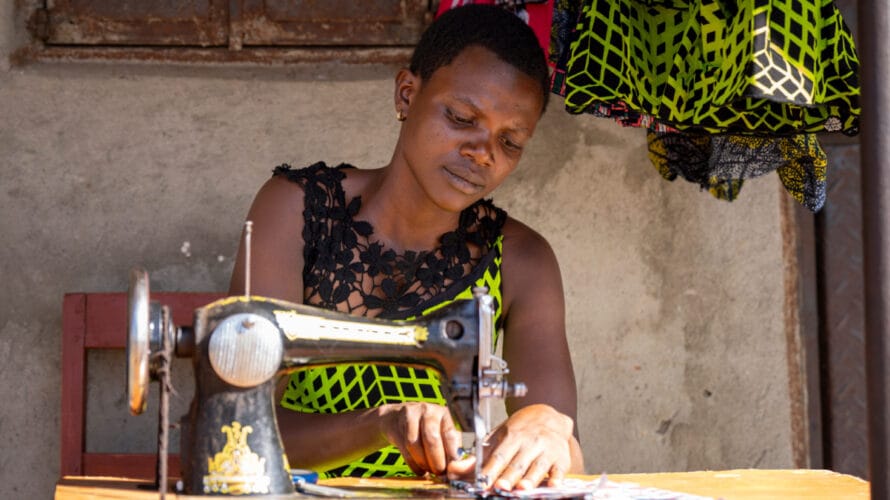 Vihreään asuun pukeutunut ugandalainen Betty oman ompelukoneensa äärellä.
