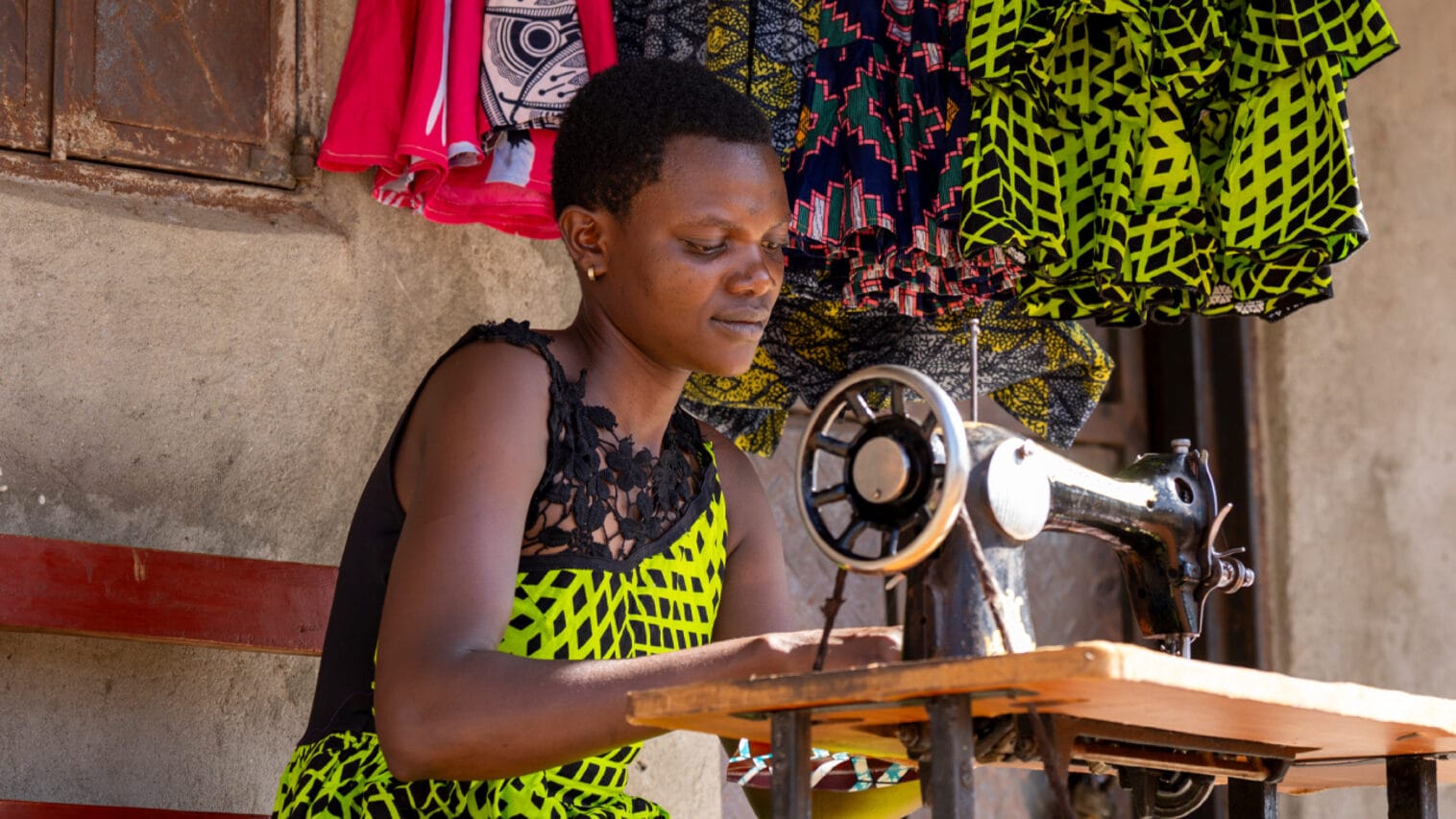 Vihreään asuun pukeutunut ugandalainen Betty oman ompelukoneensa äärellä.
