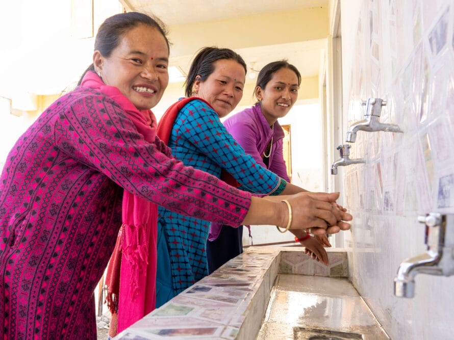 Nepalilaisia naisia kummien tuella rakennetun käsienpesupisteen luona.