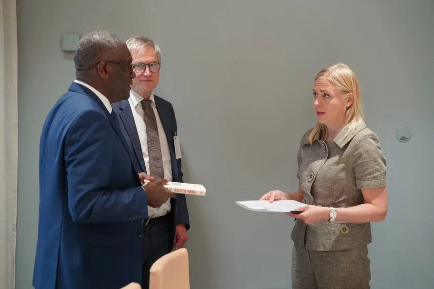 Tohtori Mukwege ja Fidan toiminnanjohtaja Harri Hakola luovuttamassa vetoomusta ulkoministeri Elina Valtoselle vihreän seinän edessä.