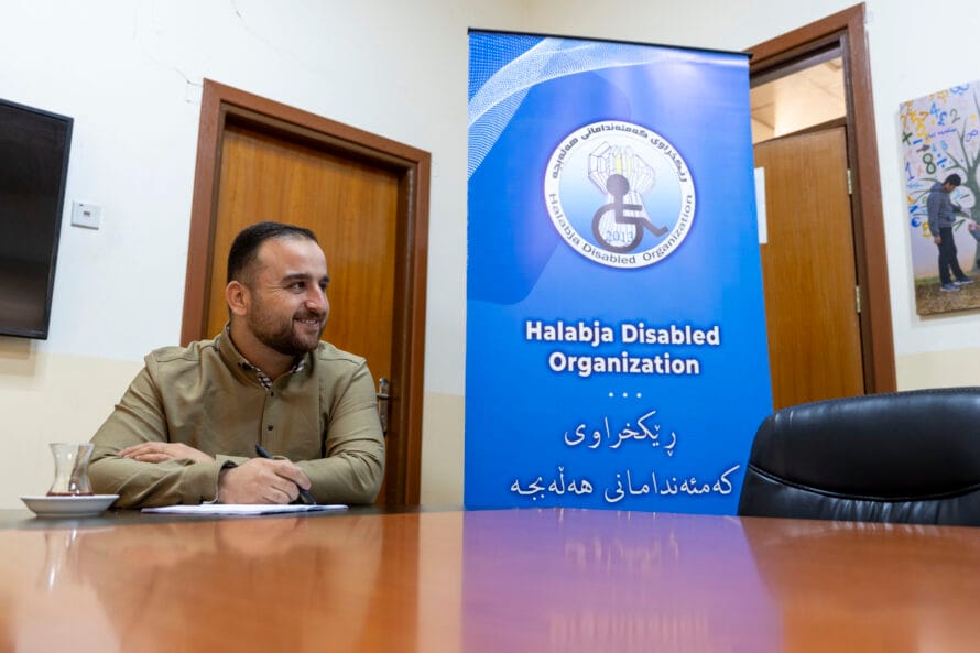 Mieshenkilö istuu pöydän ääressä edessään vihko ja kädessään kynä. Taustalla näkyy julisteessa HDO-järjestön logo.