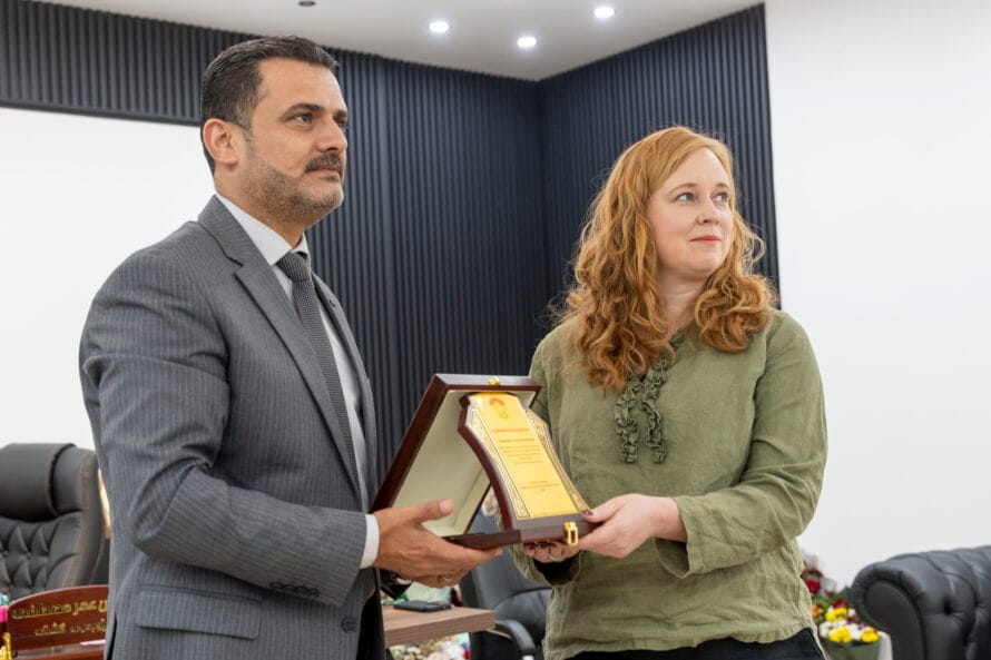 Pukuun pukeutunut mieshenkilö ojentaa naiselle kunnialaatan pitkäjänteisestä työstä.