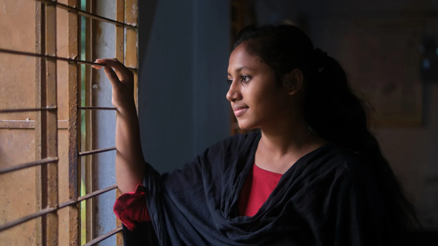 Bangladeshilainen teinityttö katsoo ikkunasta ulos.