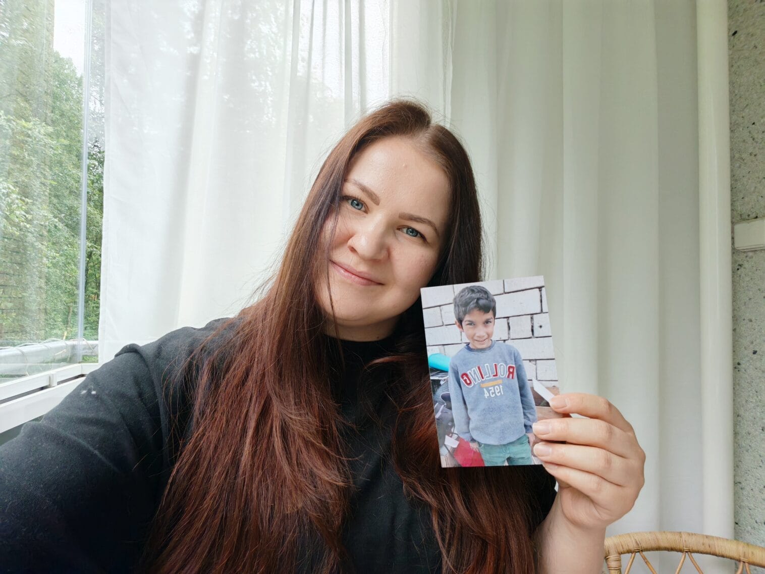 Nainen pitää valokuvaa kädessään, jossa on hänen kummilapsensa