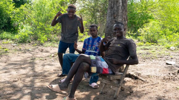 Nuoret kenialaispojat istuvat puun varjossa ja nauravat.