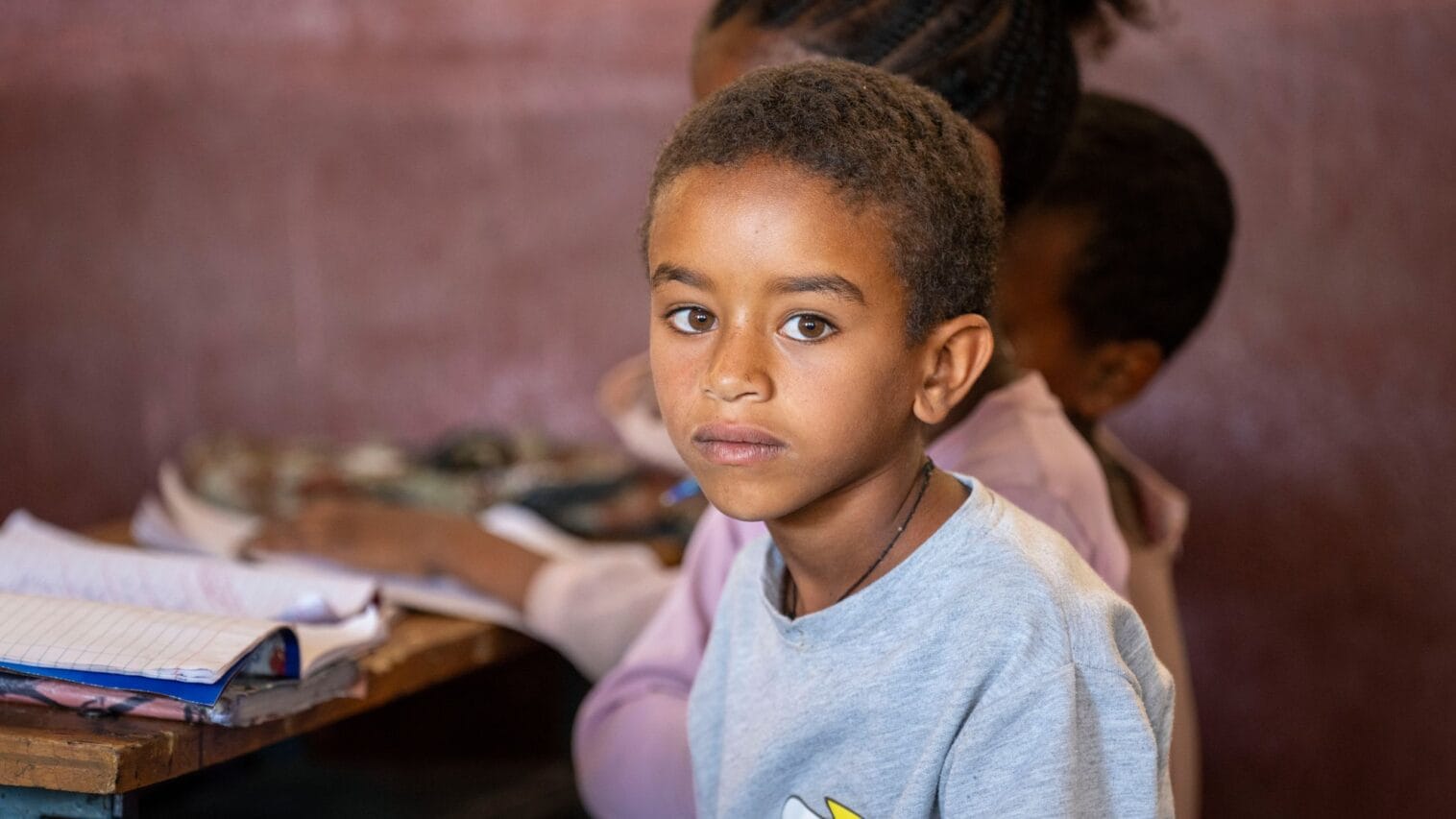 Koululaispoika istuu pulpetin ääressä ja katsoo kameraan.