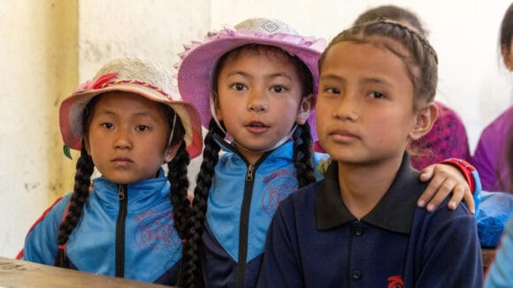 Kolme nepalilaista koulutyttöä katsoo kameraan.