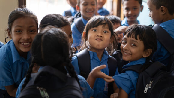 Bangladeshi children in school uniforms, backpacks on their backs, smiling and clowning around.