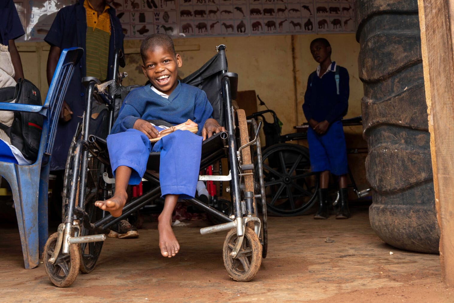 Koulupukuun pukeutunut oppilas istuu pyörätuolissa luokkahuoneessa ja hymyilee.