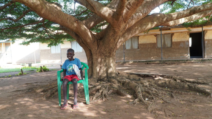 Ugandalainen poika istuu hymyillen ulkona vihreällä tuolilla.