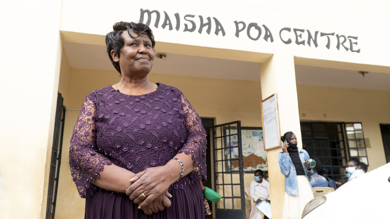 A woman stands in a purple dress front of Maisha Poa Centre.