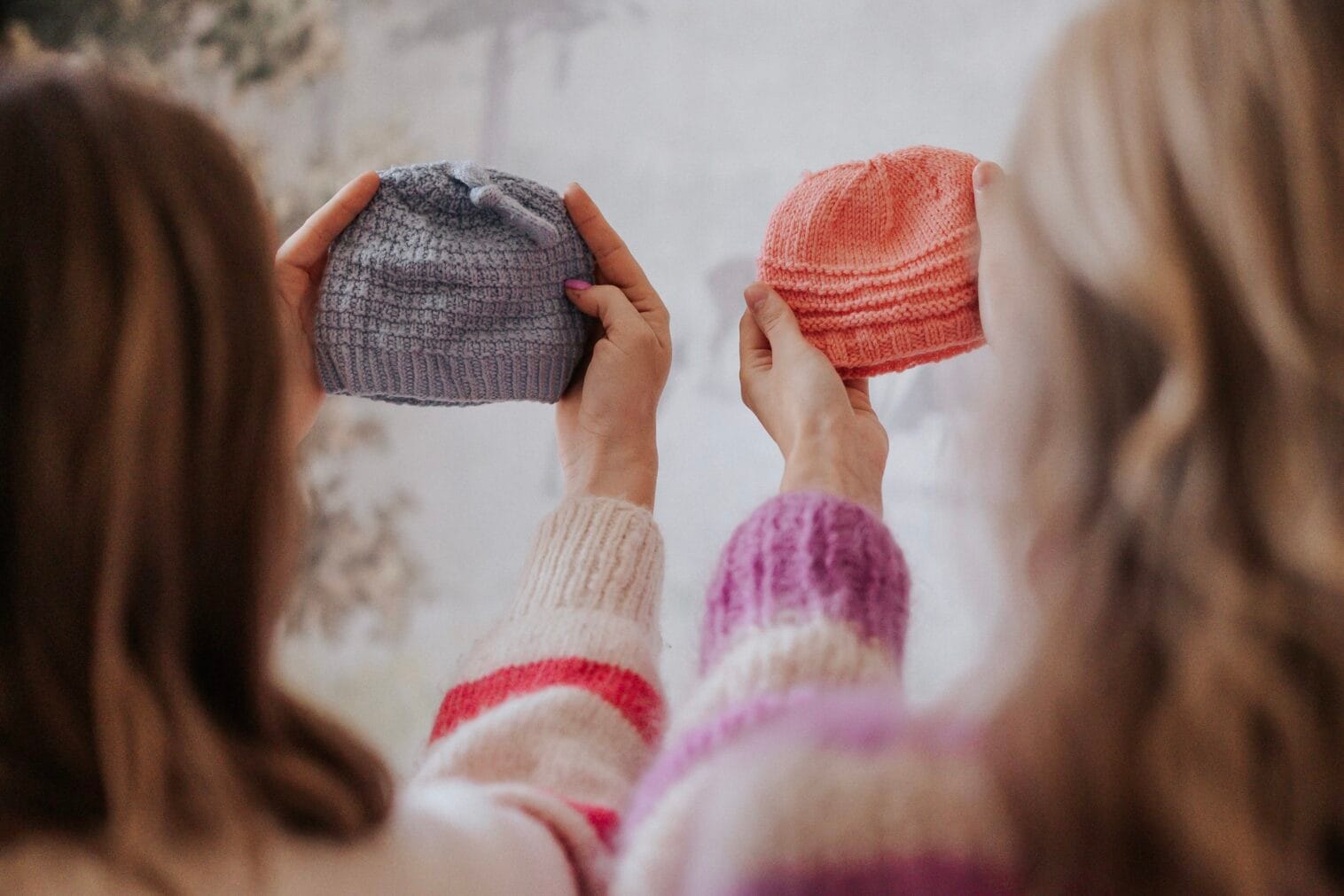 Kaksi naista pitää neulottuja pipoja käsissään