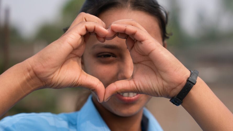 A girl forms a heart shape with her hands and peeks through it.