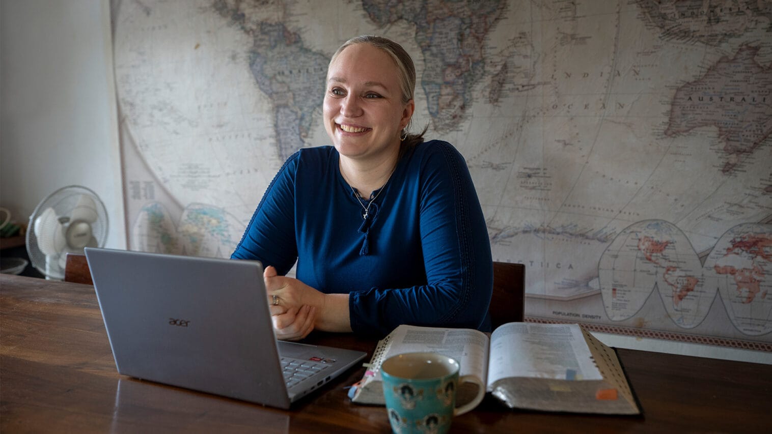 Nainen istuu pöydän ääressä, avoimen Raamatun edessä.