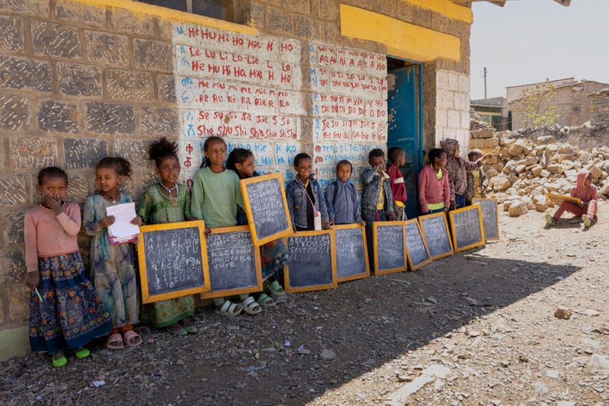 Lapset seisovat koulurakennuksen seinustalla, käsissään liitutaulut. Etiopia, Tigray.