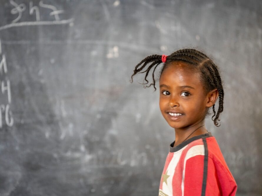 A girl stands before a chalk board.