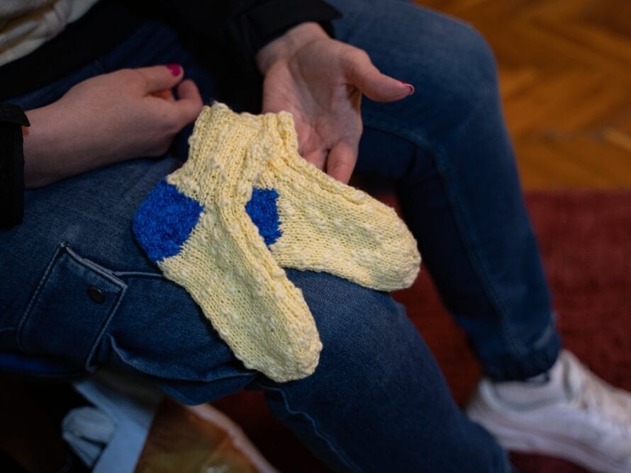 Nainen pitää sylissään käsin kudottuja villasukkia Ukrainan lipun väreissä.