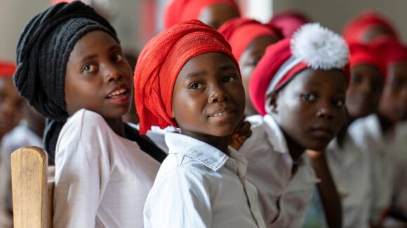 Punahuivinen kongolaistyttö hymyilee kuoron kanssa.