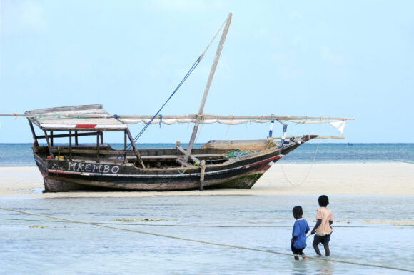 Two African children on the beach with a fishing boat in the background.