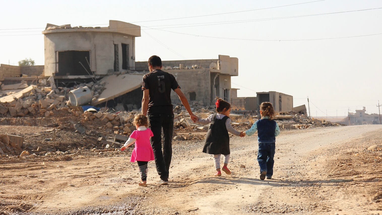 Mies kävelee lasten kanssa raunioiden keskellä.