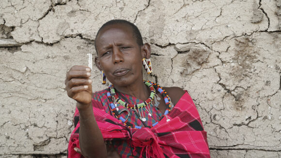 A woman sitting with pink scarf around her and a blade in her hand.