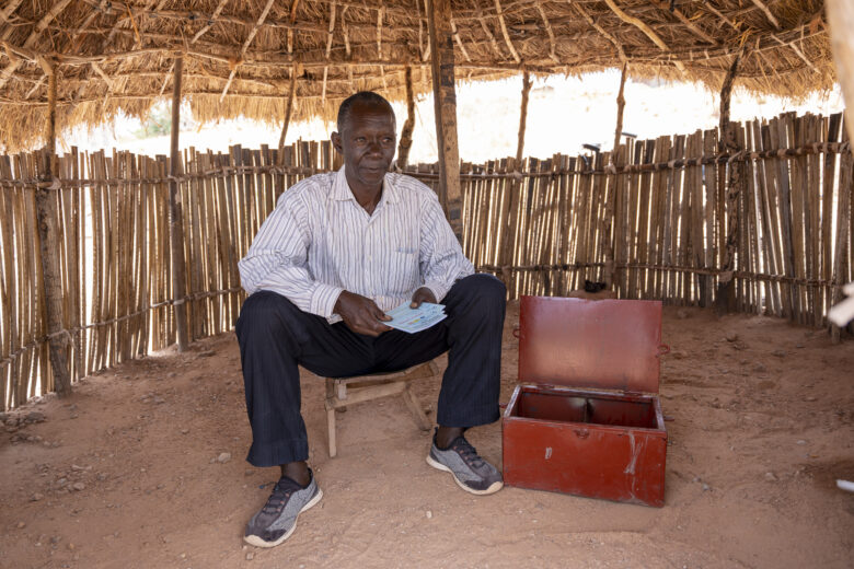 A Congolese man sits next to a red deposit box.