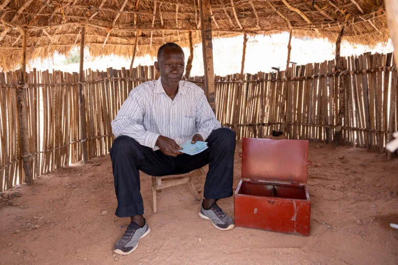 A Congolese man sits next to a red deposit box.