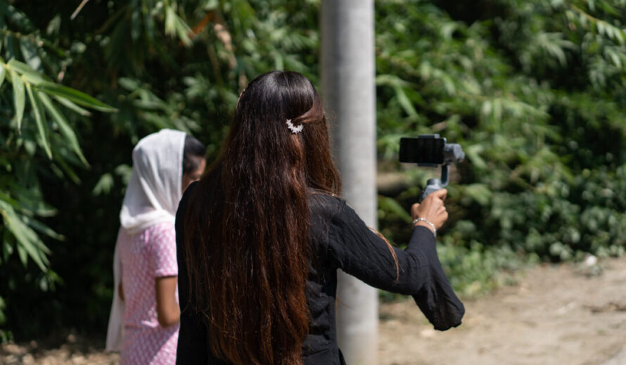 Bangladeshilainen tyttö selin kameraan ja kuvaa itseään puhelimella.