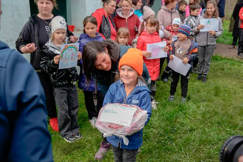Tyttö hymyilee pussukka kädessä, taustalla lapsijoukko pitelee piirrustuksia.